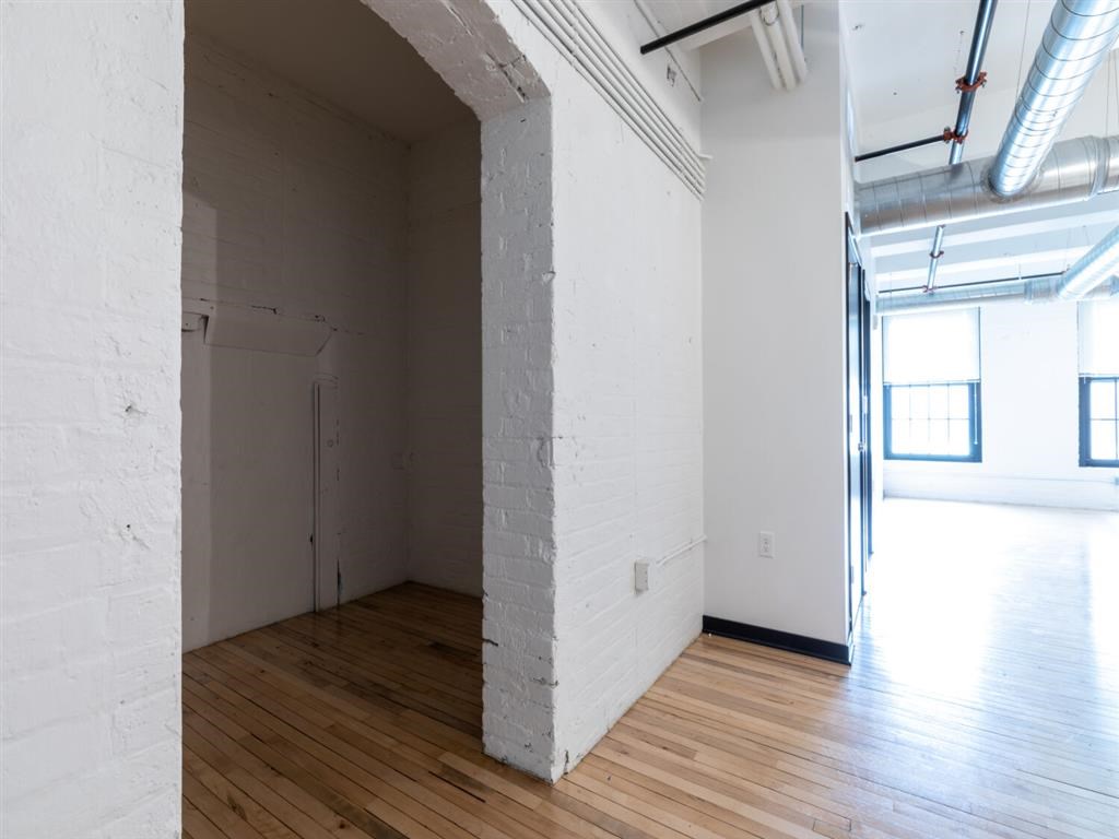 A white room with wooden floors and a doorway leading to another room.