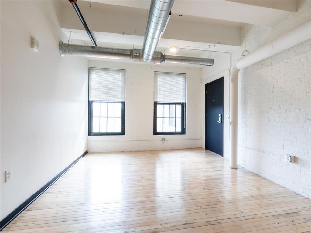 A room with wooden floors and white walls, with two windows and a door on the right side.