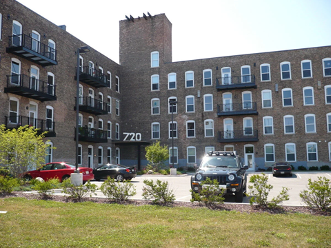 A black car is parked in front of a brick building with the number 7720 on it.