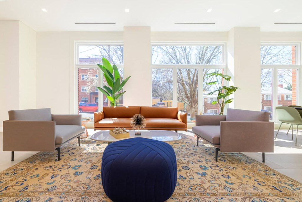 A living room with a blue ottoman in the middle of a rug.at The Vale at the Parks, Washington, DC  