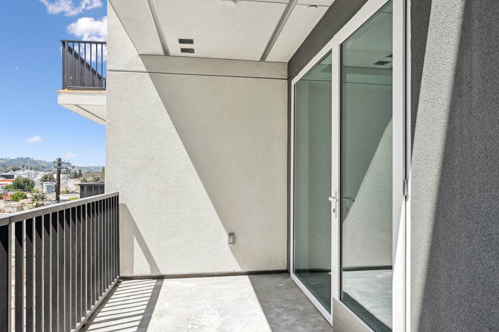 A balcony with a glass door and a metal railing at Coro Apartments, Los Angeles, CA 90016