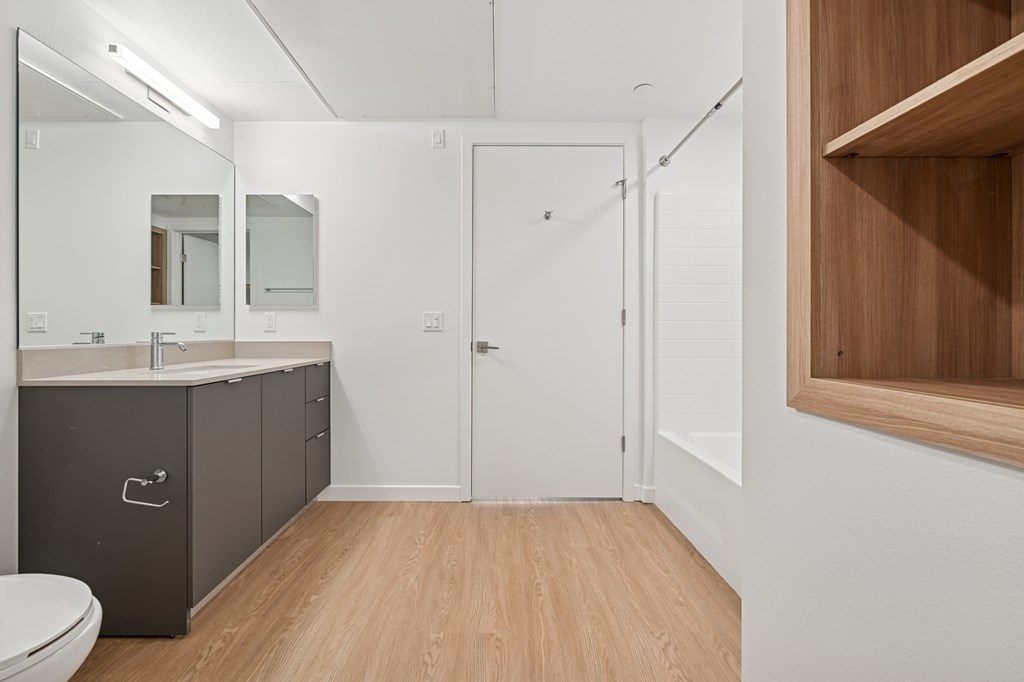 A bathroom with a toilet, sink, and mirror at Coro Apartments, Los Angeles, CA
