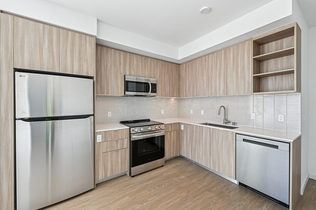 A kitchen with a refrigerator, oven, microwave, and sink. at Coro Apartments, Los Angeles, California