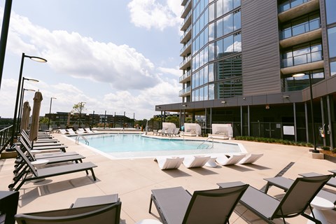 A pool area with sun loungers and a tall building in the background.