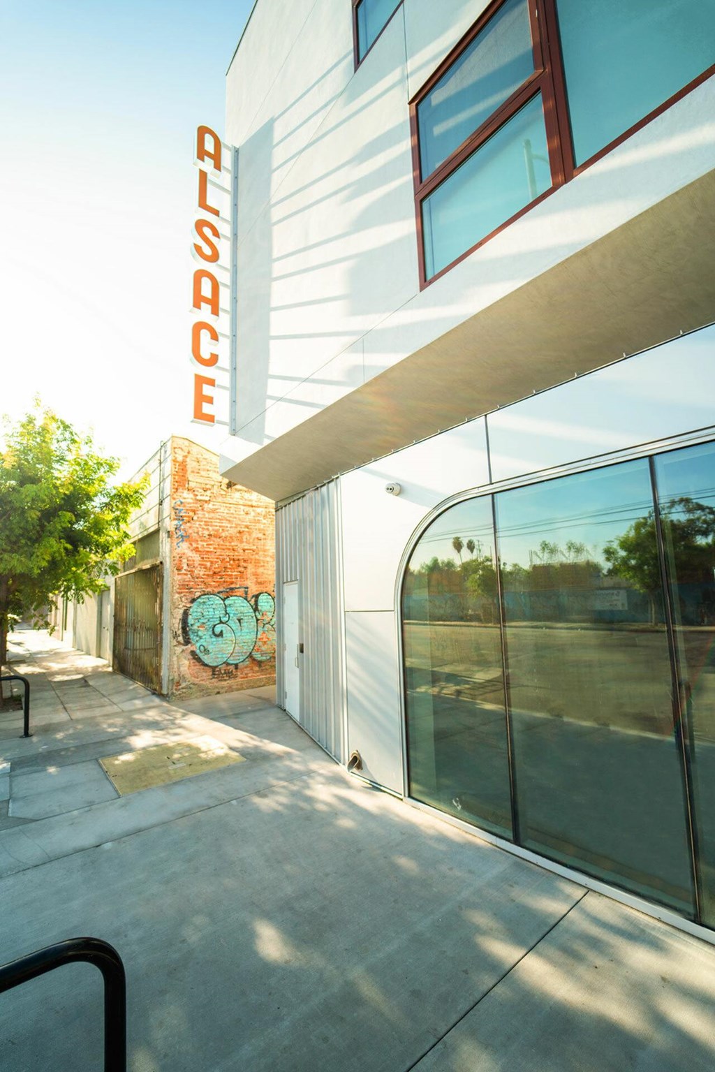 A modern building with a glass facade and a red brick wall with a mural on it.