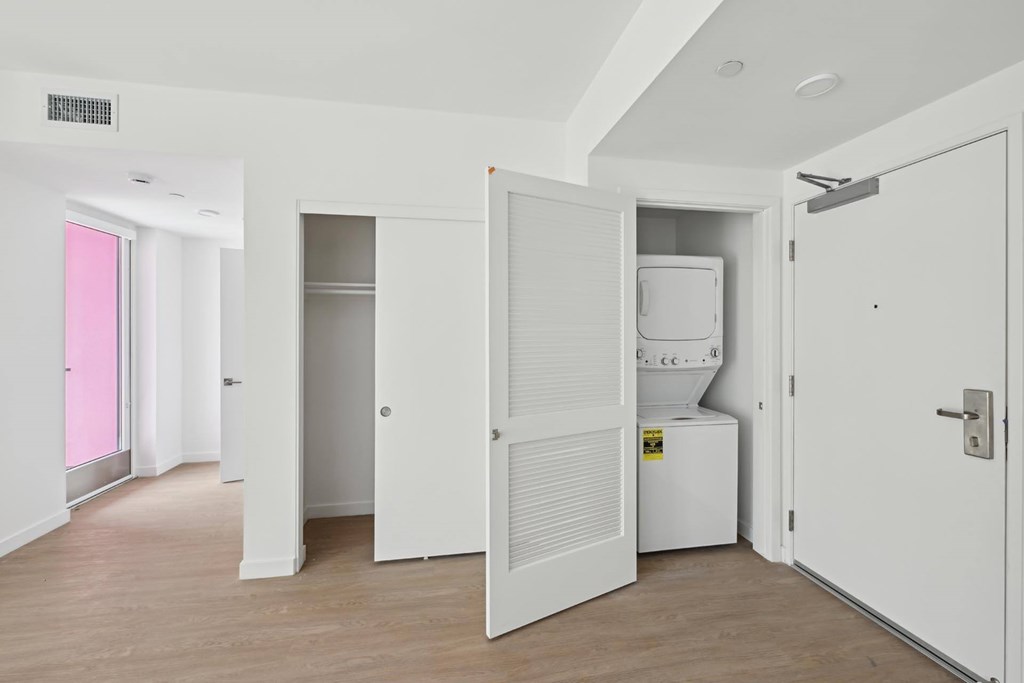 A white room with a pink door and a white fridge.