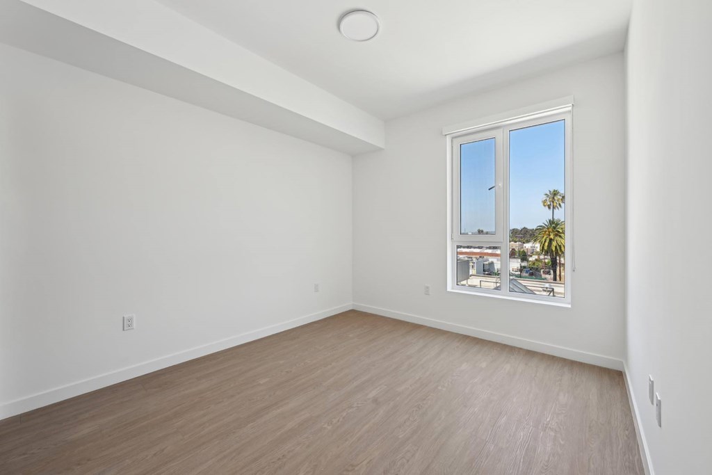 Empty room with a window showing a view of palm trees and a building.