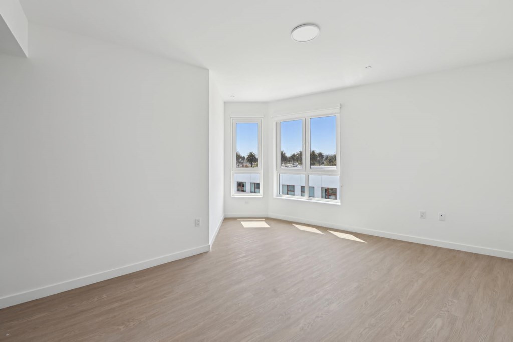 A room with white walls and wooden flooring, with a large window and pictures on the wall.