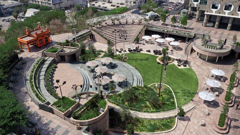 A large, circular, outdoor seating area is surrounded by a grassy hill and a building.