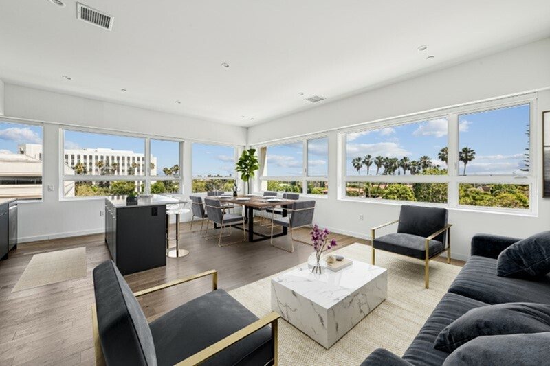 A modern living room with a large marble coffee table and a view of the outdoors through the windows.