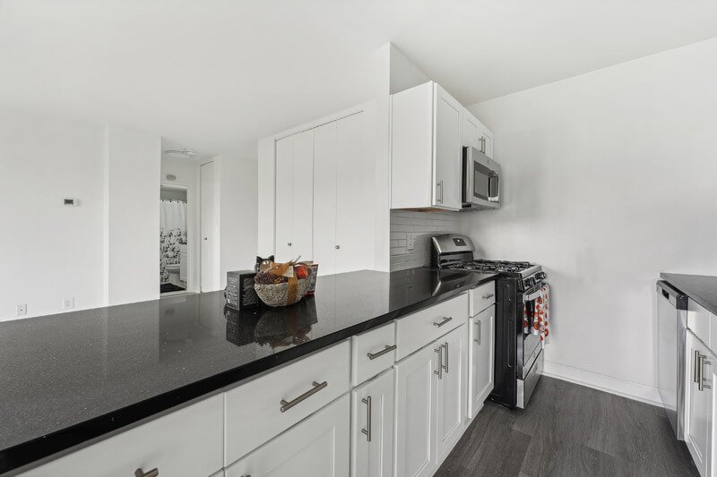 A kitchen with white cabinets and black countertops.