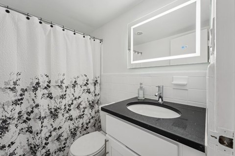 A bathroom with a floral shower curtain, a white toilet, a black countertop, and a white sink.