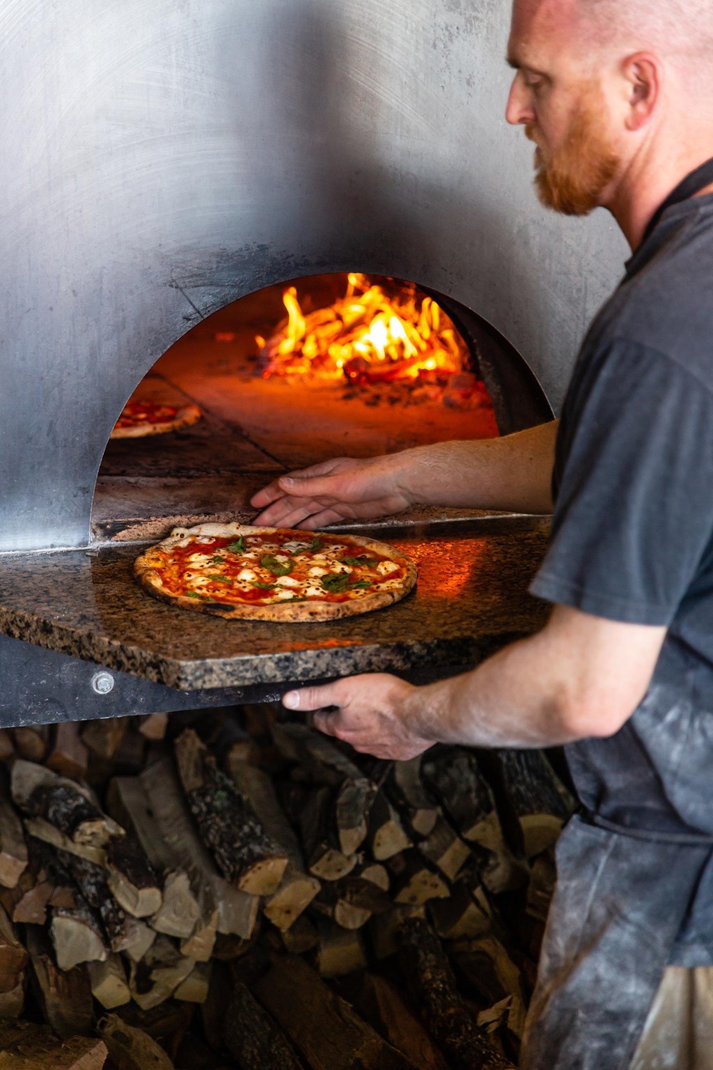 A man is making pizza in a wood-fired oven.at Channel House, Oakland, 94607