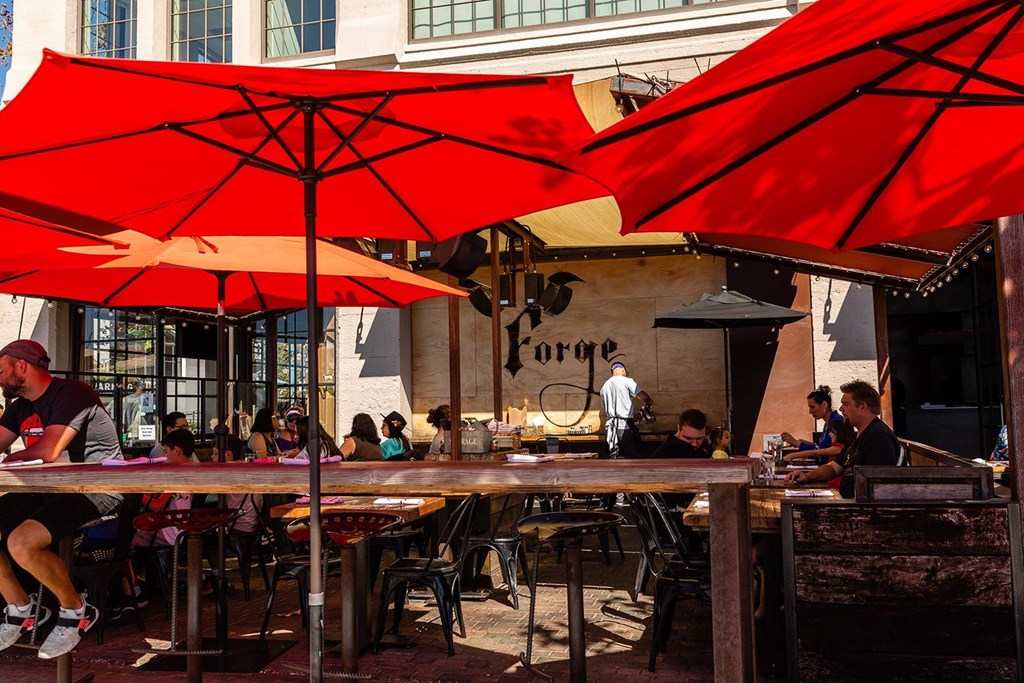 A restaurant with red umbrellas and people sitting at tables.at Channel House, Oakland California