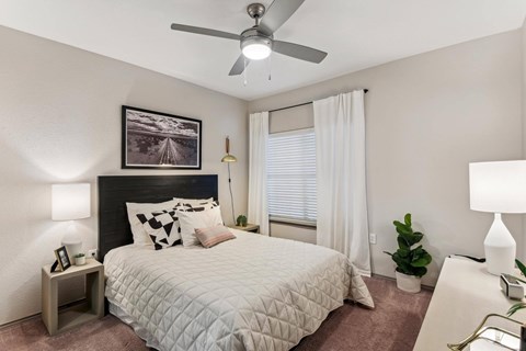 A bedroom with a bed, a ceiling fan, and a painting on the wall.
