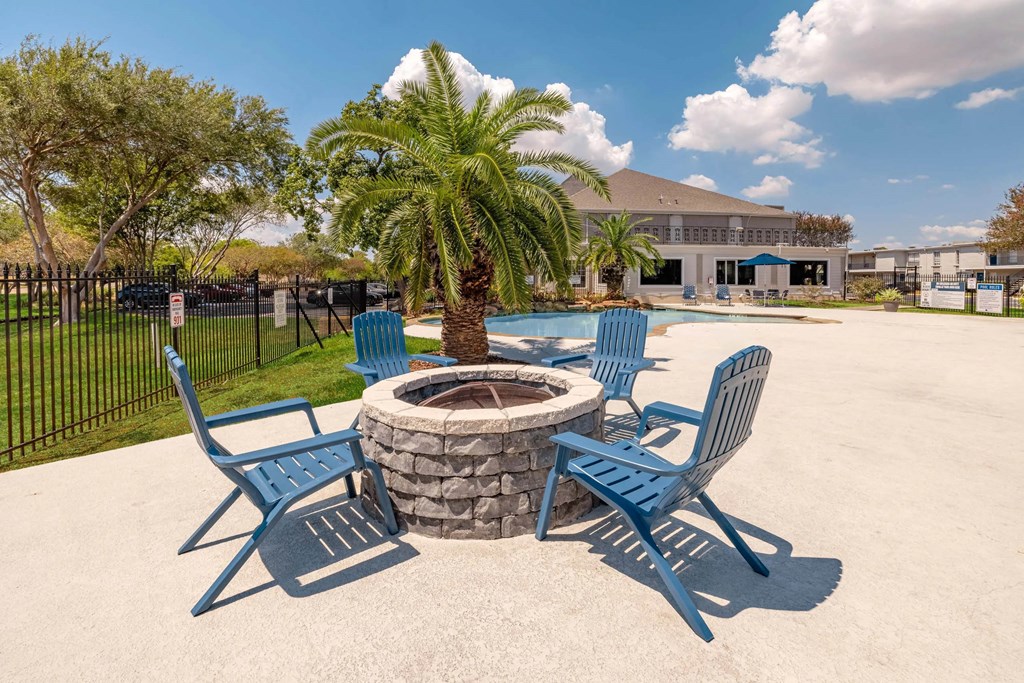 A fire pit surrounded by blue chairs in a sunny outdoor setting.