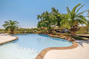 A large outdoor swimming pool surrounded by palm trees and a fence.