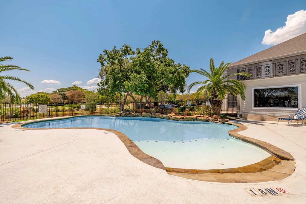 A large outdoor swimming pool surrounded by trees and a building.
