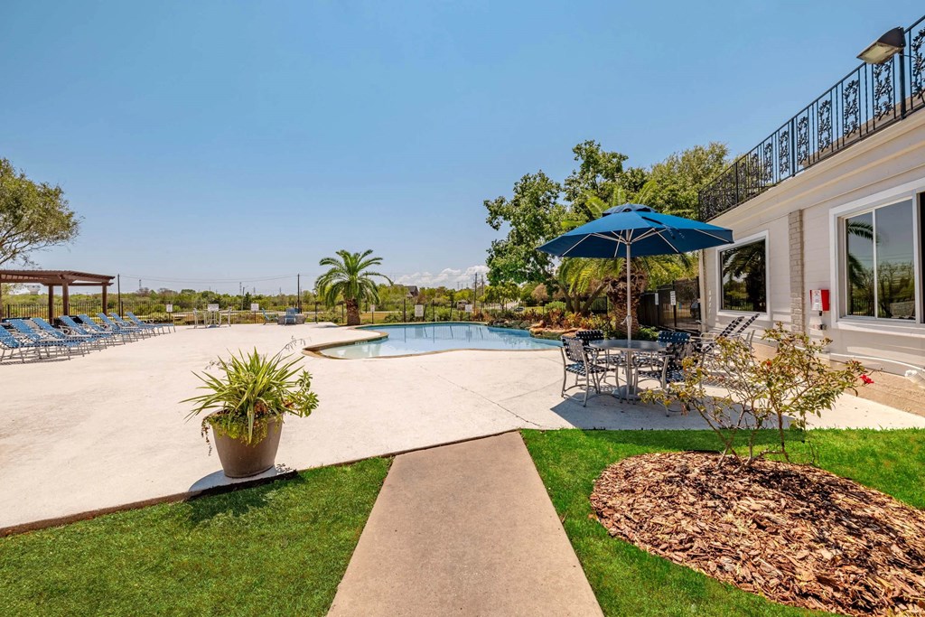 A pool area with a blue umbrella and a concrete walkway.
