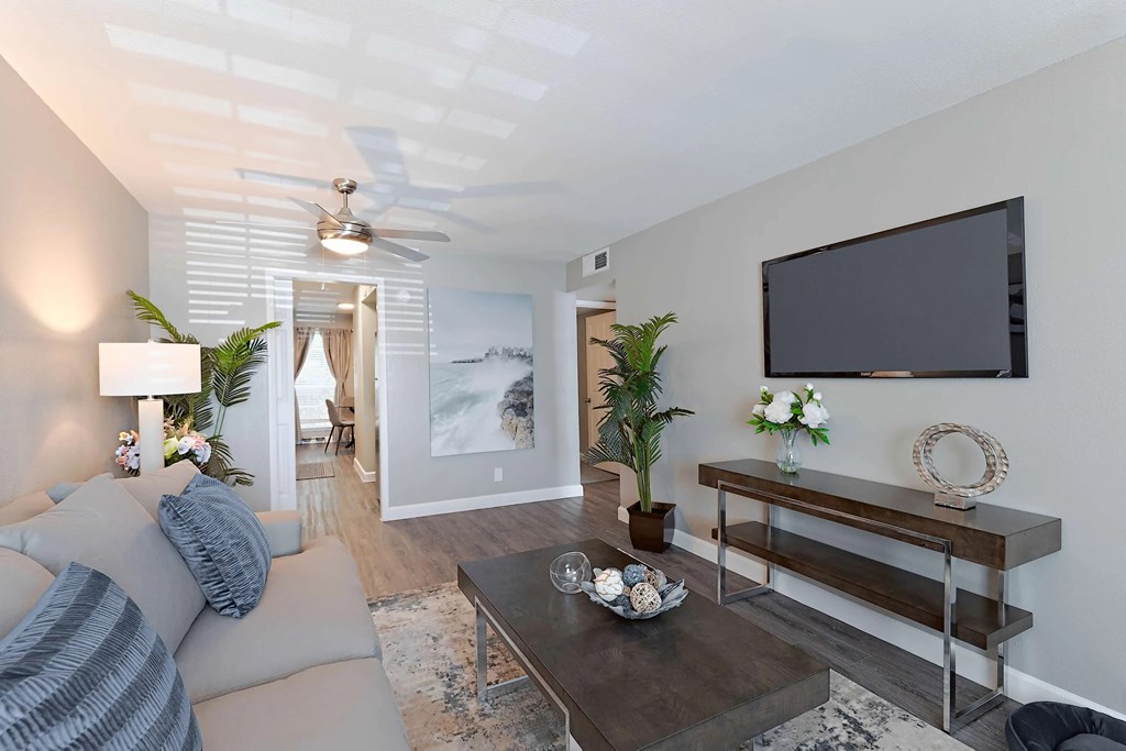 A modern living room with a grey couch, a coffee table, a flat screen TV, and a ceiling fan.