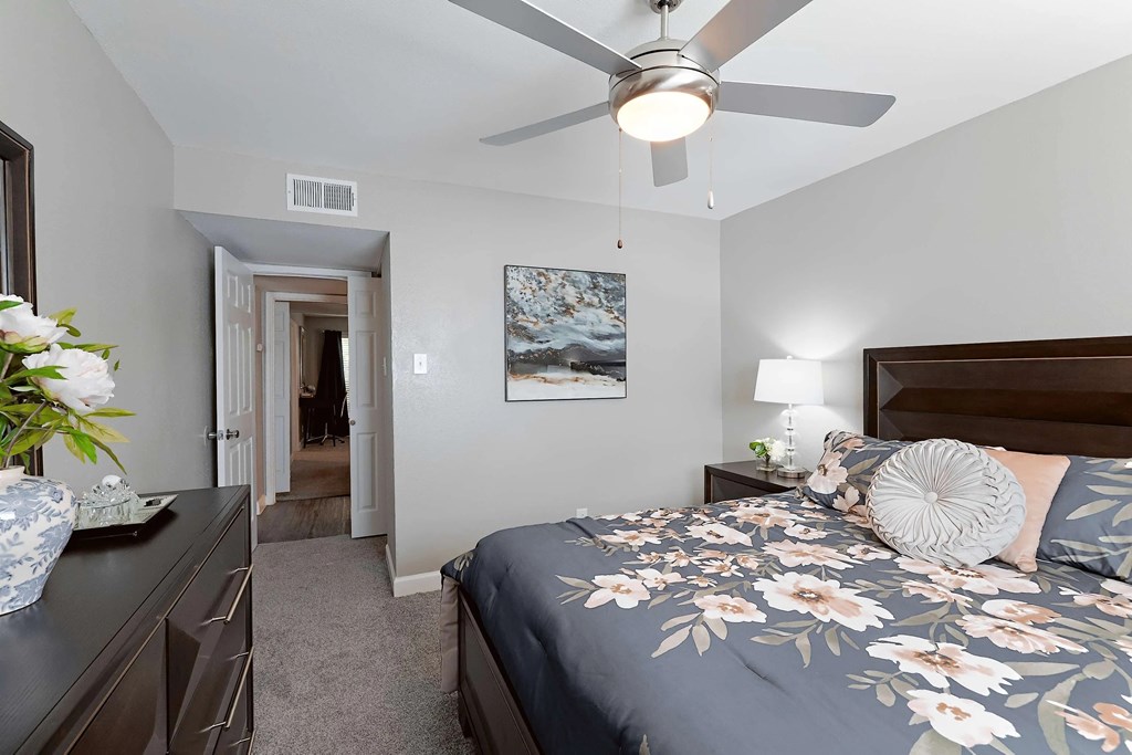 A bedroom with a bed, a ceiling fan, and a painting on the wall.