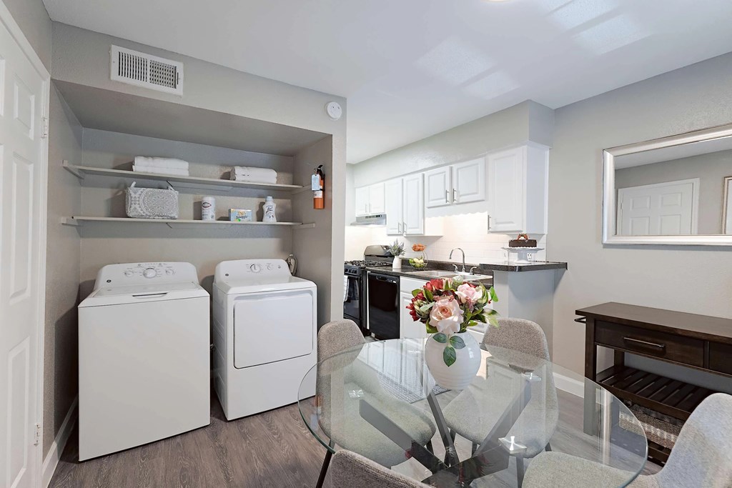 A laundry room with a washer and dryer, a dining table with chairs, and a kitchen area with cabinets and a countertop.