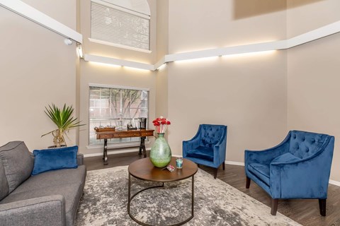 A living room with a grey couch, a blue armchair, and a coffee table with a green vase on it.