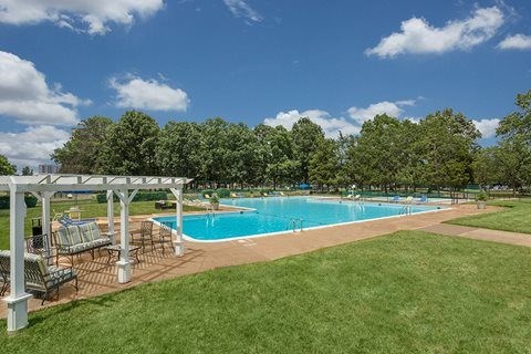 A pool surrounded by a grassy area and trees.