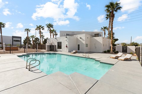 A swimming pool in front of a house with a fence and palm trees.