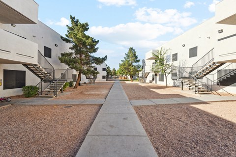 A long concrete walkway separates two rows of white buildings with trees in between.