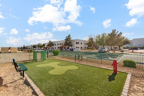 A playground with a green bench, a red fire hydrant, and a tennis court.