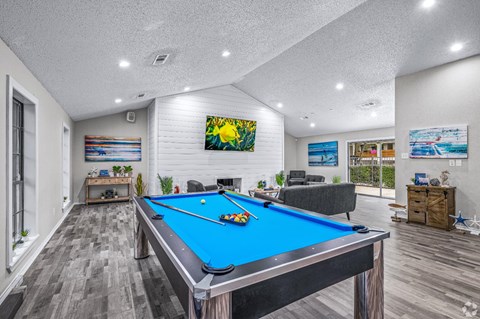 A pool table is in the middle of a room with a couch and a painting on the wall.