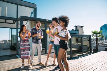 Four people are standing on a wooden deck, enjoying drinks and conversation at Coro Apartments, Los Angeles, CA