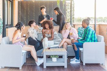 A group of people are sitting on a patio with a woman standing behind them at Coro Apartments, Los Angeles, CA 90016