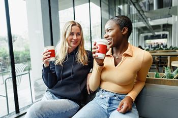 Two people sitting on a bench with coffee cups at Coro Apartments, Los Angeles, California
