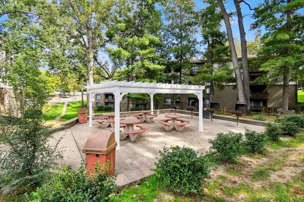 A picnic area with tables and a pavilion is surrounded by trees.