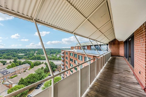 A balcony with a metal railing overlooks a parking lot and buildings.