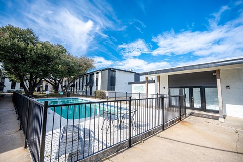 A pool surrounded by a black fence with a building in the background.