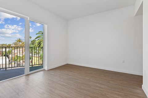 A room with a sliding glass door leading to a balcony with a view of a fence and trees.