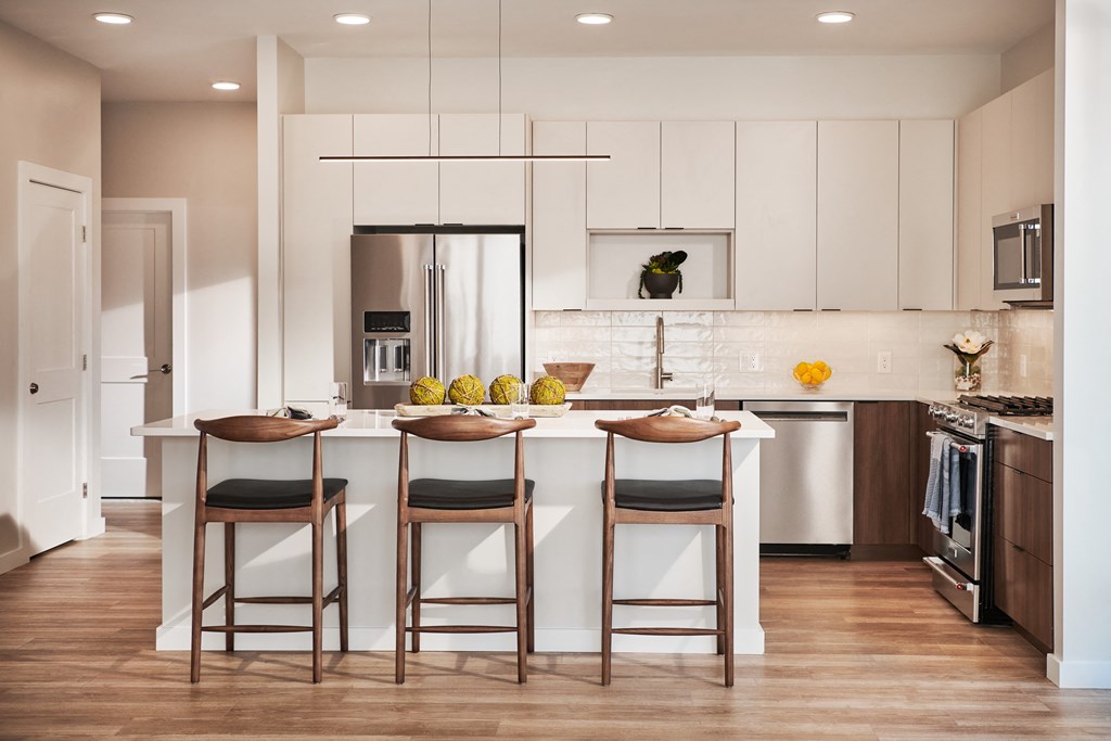 a kitchen with white cabinets and a white island with three chairs
