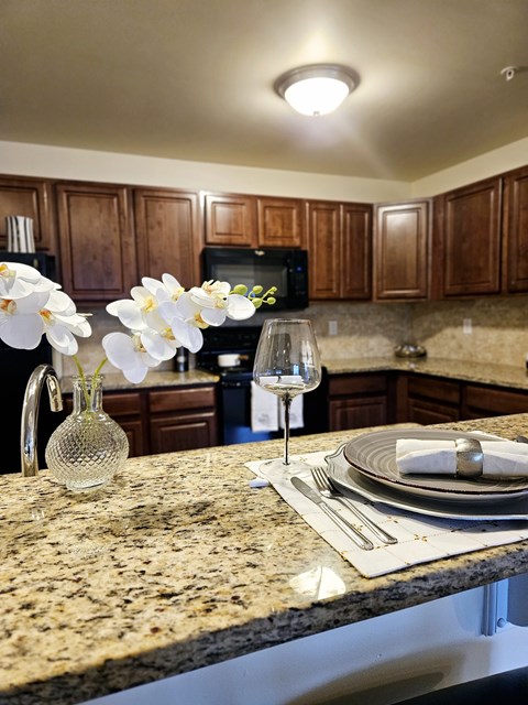 A kitchen counter with a wine glass, a vase with white flowers, and a plate set for two.