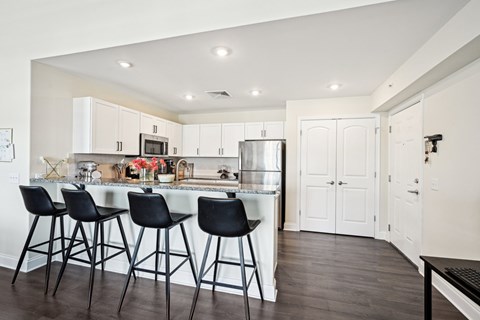A kitchen with white cabinets and black bar stools.