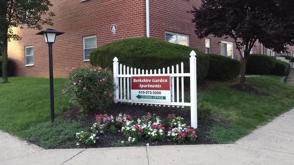 a white garden gate sign in front of a red brick building