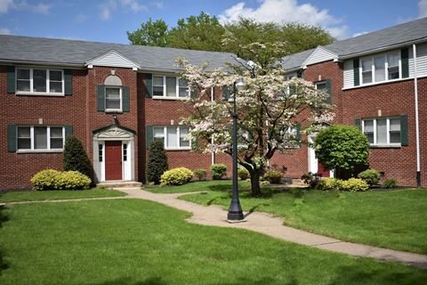 a red brick apartment building with a green lawn and flowering tree in front of it