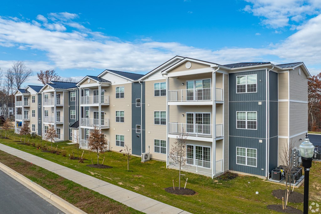 A row of modern apartment buildings with balconies and trees in front.
