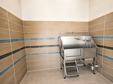 A stainless steel table is in a room with tan tile walls.