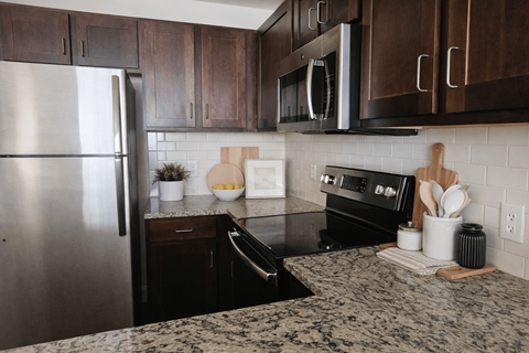 A kitchen with a stainless steel refrigerator and black countertops.