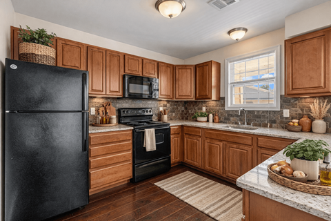A black fridge sits in a kitchen with wooden cabinets and a stone backsplash.