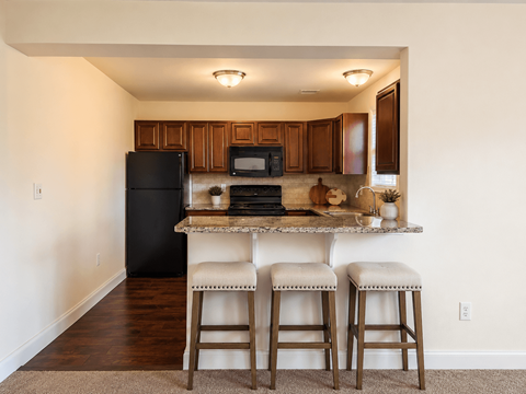A kitchen with a black refrigerator, a microwave, and a counter with two stools.