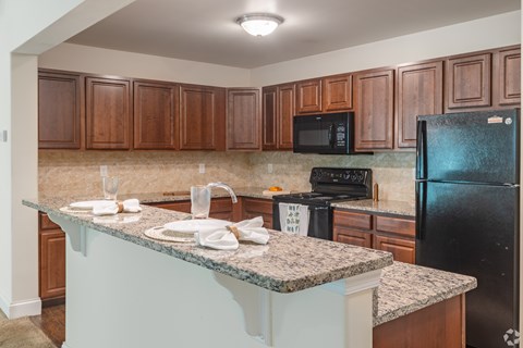 A kitchen with a black refrigerator and brown cabinets.